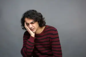 Person experiencing tooth pain and discomfort near the gum line, an early sign of gum recession.